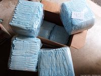 6 packages of large size adult diapers, wing style, stacked in and around an open cardboard box.