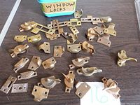 Top-down view showing multiple brass window locks and lock plates spread on a table, with a container labeled 'Window Locks' in background.