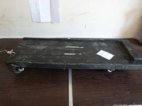 Top view of black plastic mechanics creeper with slight wear and scratches, showing flat surface and wheel assembly underneath.
