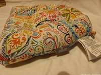 Close-up of one square chair cushion showing colorful floral and paisley pattern with attached ties and label 'pillow'.