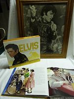 Wide photo showing both the large framed Elvis Presley photo and the collectible book with open pages displayed.