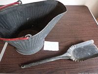 Photo showing black metal fireplace ash bucket with red handle and metal scoop, both with visible signs of use.
