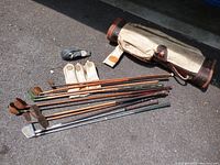 Photo showing the complete set of wooden golf clubs laid out next to the vintage canvas and leather golf bag, along with several headcovers.