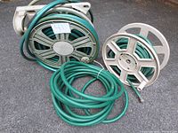 Three green garden hoses, two on plastic reels with wheels, one loose on ground