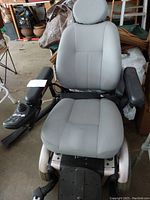 Front view of motorized wheelchair, gray vinyl seat with headrest, joystick control on right armrest, front casters and rear drive wheels