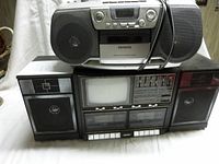 Photo showing two boom boxes stacked, with Panasonic on bottom featuring CRT screen and Aiwa on top in silver