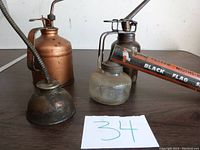Four antique oil cans and sprayer on a wood table with '34' card in front.