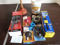 Photo showing the full lot of various plumbing supplies including a red plunger, multiple Korky brand toilet flappers, an adjustable fill valve, a blue washer, a tank-to-bowl rubber washer, and a yellow box fill valve.