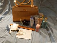 Full lot showing brown Etienne Aigner shoulder bag with assorted Estee Lauder skincare tubes, perfume bottles, perfume sampler vials, and a wooden ruler.