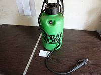 Green Spray Dog pump sprayer with black hose and spray nozzle on a wooden table