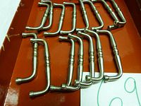 Fifteen stainless steel cabinet drawer pulls arranged in a red box, showing curved handles with decorative rings.