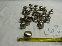 Photo showing the collection of 26 stainless steel brushed silver round cabinet knobs scattered on a white surface with a measuring tape displaying approximately 1 inch diameter knob.