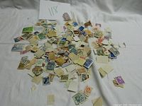 Overview photo showing a large assortment of loose canceled postage stamps scattered on a white surface with small paper backing pieces attached