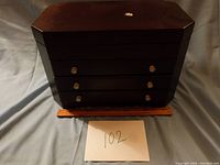 Closed view of dark brown wooden jewelry box with three drawers, small round knobs, price tag sticker remnant on top.