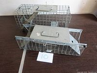 Two metal live animal traps shown side by side on a wooden surface with a label marked '10' in front.