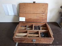 Open view of vintage wooden box showing multiple compartments filled with various nails including concrete nails.