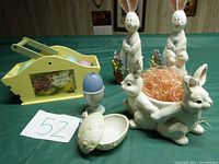 Entire lot items displayed together on green table cloth, showing wooden bunnies, ceramic candle holder, wooden basket with plastic eggs, and egg holder with candle
