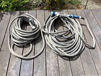 Two no kink garden hoses coiled on a wooden surface outdoors, showing full length and attachments.