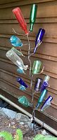 Full view of the bottle tree against a brown wood-paneled background showing multiple colored glass bottles including red, green, blue, and clear bottles arranged on the metal branches.