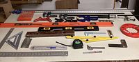 Wide shot of various clamps, levels, measuring tapes and marking tools arranged on table.