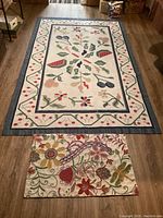 Both colorful rugs shown together on wood floor; larger one has fruit motifs, smaller one floral.