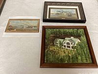 Three artworks displayed on a white surface: large framed house painting by CV Bailey, framed maritime print, and an unframed maritime print.