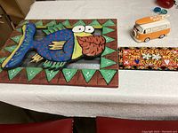Photo showing all three items in the lot together on a table: fish wall art, NOLA sign, and VW bus ceramic bank.