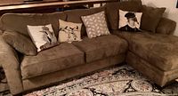 Full view of taupe two-piece sectional couch with multiple throw pillows on a patterned rug