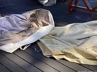 Two large beige canvas covers loosely laid on outdoor deck floor showing their size and fabric texture.