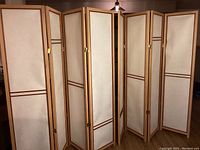 Both room dividers side by side showing four panels each, standing upright with parchment panels framed by blonde oak wood and darker trim.