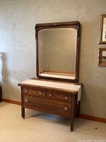 Front and side view of vintage oak dresser with crystal knobs and large beveled mirror with carved scroll frame leaning on it.