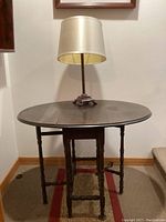Front view of the oval-folded vintage wooden table with lamp on top showing table surface and lamp shade.