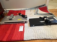 Overview of two media players: Pioneer DVD player silver with remote, Panasonic Blu-ray black with remote, placed on quilted blanket.