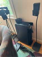 Four Bose stand speakers on stands with one speaker visibly cracked, Bose Acoustimass bass module standing vertically on the floor, speaker wires coiled nearby.