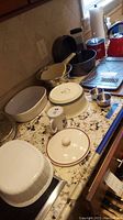 Photo showing various kitchen items including OXO teakettle, Wilton Bundt pan, Pfaltzgraff bowl, Corning French White glass containers, cookie sheets, metal colander and Kuhn Rikon pot on kitchen counter.