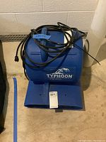 Front view of blue Typhoon floor blower dryer with power cord wrapped on top, sitting on concrete floor.