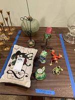 Lot arranged showing frog-themed pillow, ceramic teapot, metal enameled frogs, and card holder, along with other brass candlesticks for scale.