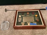 Golf putter laying behind shadow box showing nine golf ball samples representing golf ball development history.