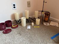 Longaberger metal candleholder with six battery-operated candles, three additional battery candles in front, two burgundy pottery pieces with lids, all displayed on carpet.