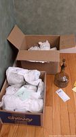 Two boxes containing stemware wrapped in white paper and a smoky crystal decanter with stopper on the floor.