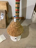 Full view of bird house on concrete floor showing roof and base