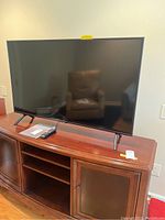 Front view of Samsung 50-inch flat screen TV on wooden TV stand, remote and manual are on the stand.