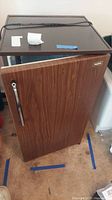 Photo of closed mini-fridge with brown woodgrain exterior and chrome handle.
