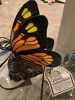 Side view showing orange and yellow stained glass butterfly wings with metal rose base and power cord with plug.