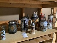 Shelf display showing seven steins and four miniature mugs
