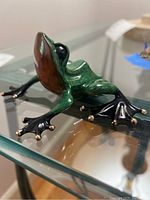 Side view of green and black enamel frog figurine on glass table
