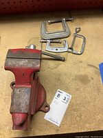 Front view of red Craftsman bench vise with three metal clamps on workbench.