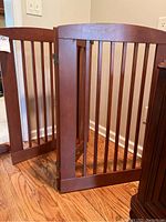 Two wood gates with vertical slats made of medium brown wood, positioned partially open on a hardwood floor.