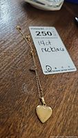 Full view of 14kt gold chain and heart pendant with monogrammed locket on wood surface