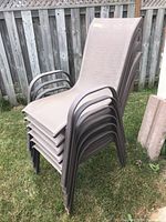 Stacked six outdoor patio chairs on a grassy lawn next to a fence. Showing the overall set and chair structure.